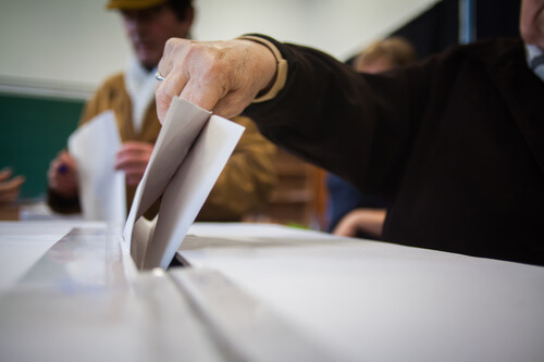 Une personne met un bulletin de vote dans une urne pour des élections.