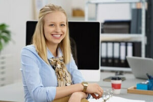 Une femme souriante se tient devant un ordinateur.
