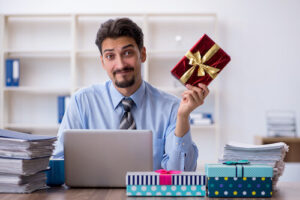 homme au bureau qui montre un cadeau devant son ordinateur en faisant une grimace