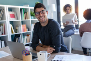 Un homme et une équipe en arrière plan sourit en utilisant un ordinateur.