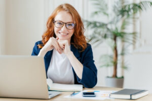 Une femme se tient devant un ordinateur et un cahier ouvert.