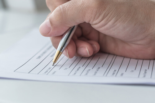 Une main tenant un stylo remplit un papier administratif qui pourrait être un PV pour les élections du CSE.